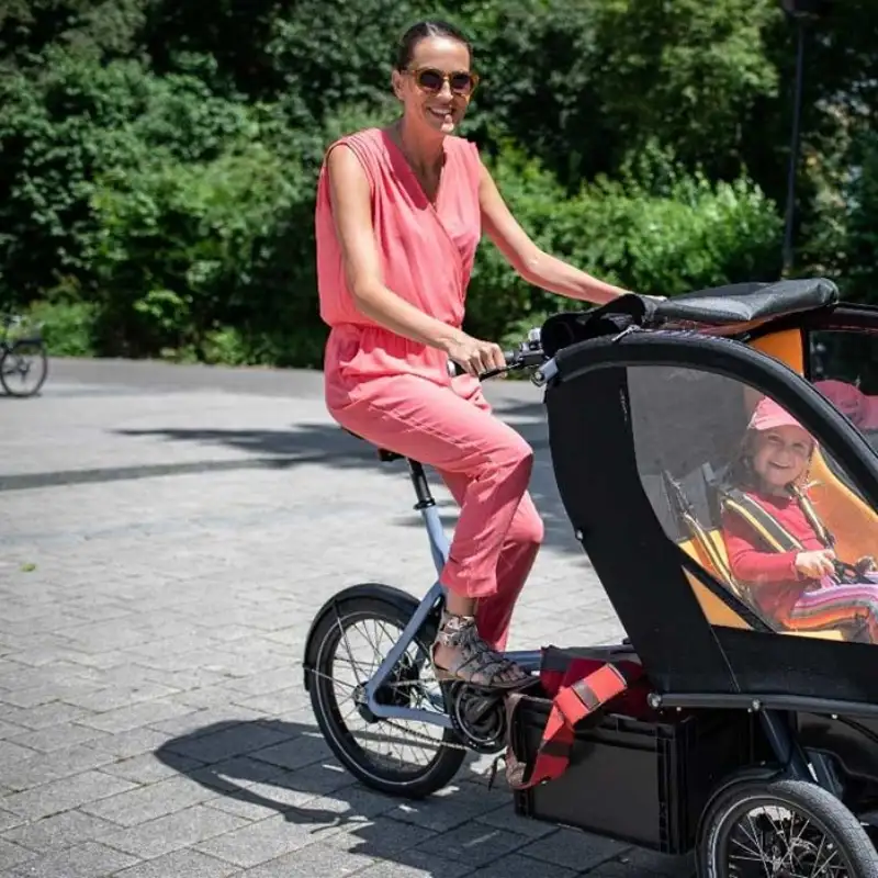 Eine Mutter fährt das Chike e-Bike in der Stadt. Ihr Kind sitzt angeschnallt darin. Beide lachen
