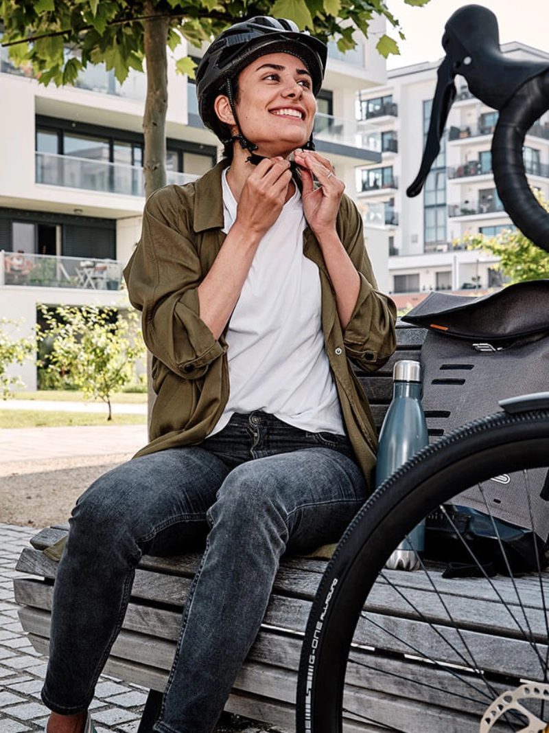 Eine Frau mit Helm sitzt auf einer  Bank unter einem Baum