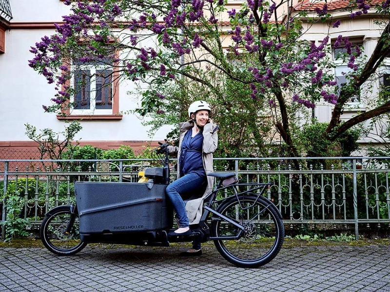 Eine JobRadlerin auf dem Lastenrad blickt zurück auf ihr Handy Eine JobRadlerin auf dem Lastenrad blickt zurück auf ihr Handy