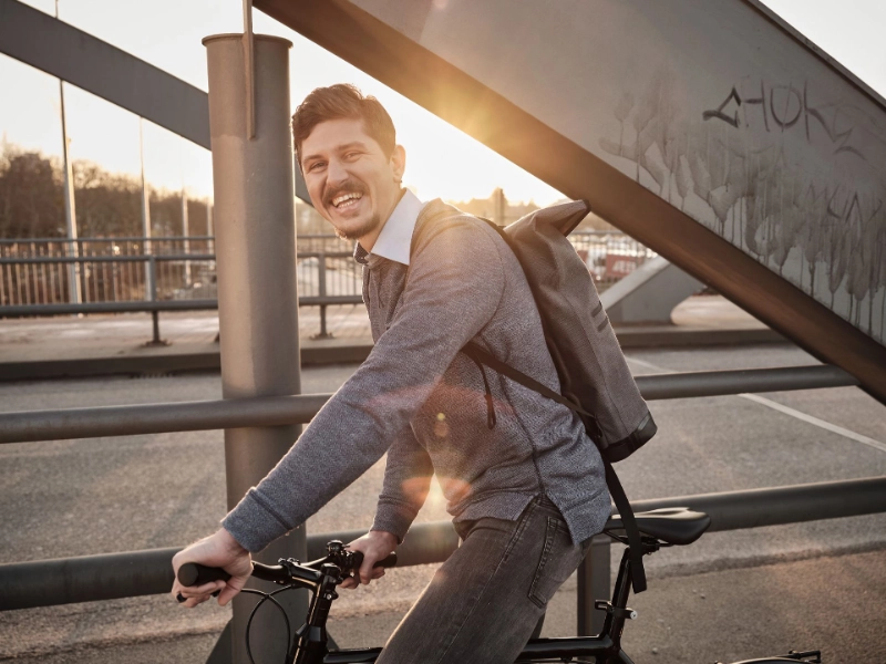 Ein lachender JobRadler fährt im Sonnenuntergang über eine Brücke