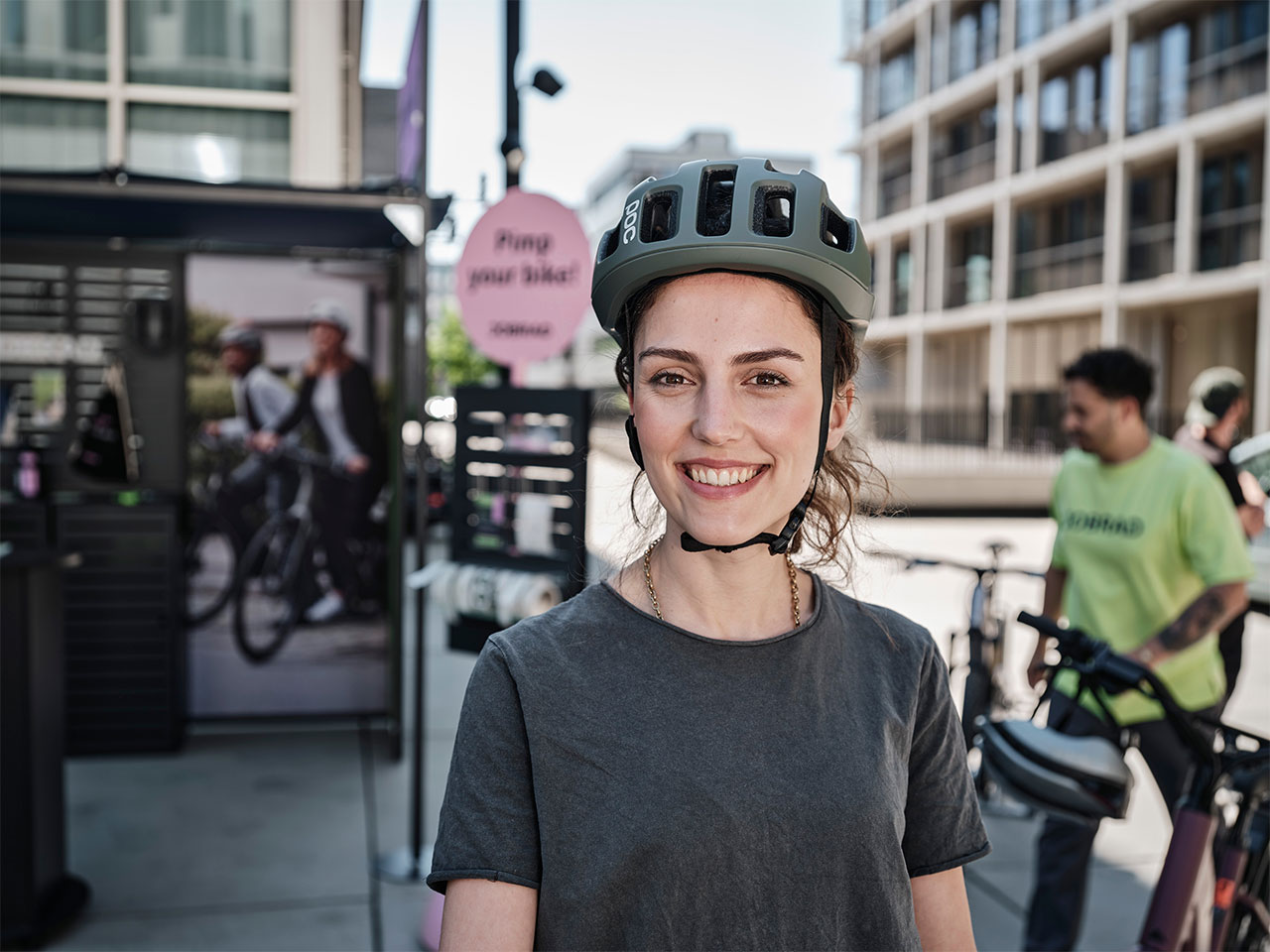 Frau mit Helm auf dem Kopf schaut lächelnd in die Kamera vor Probefahrrädern